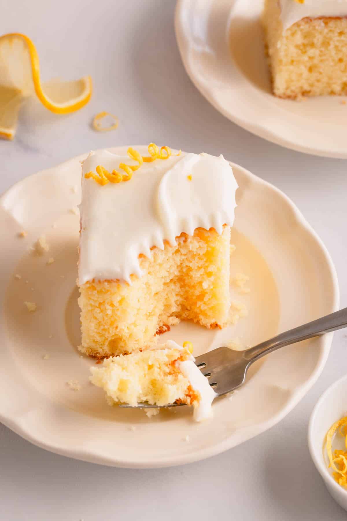 A slice of frosted lemon sheet cake on a plate with a fork holding a bite.