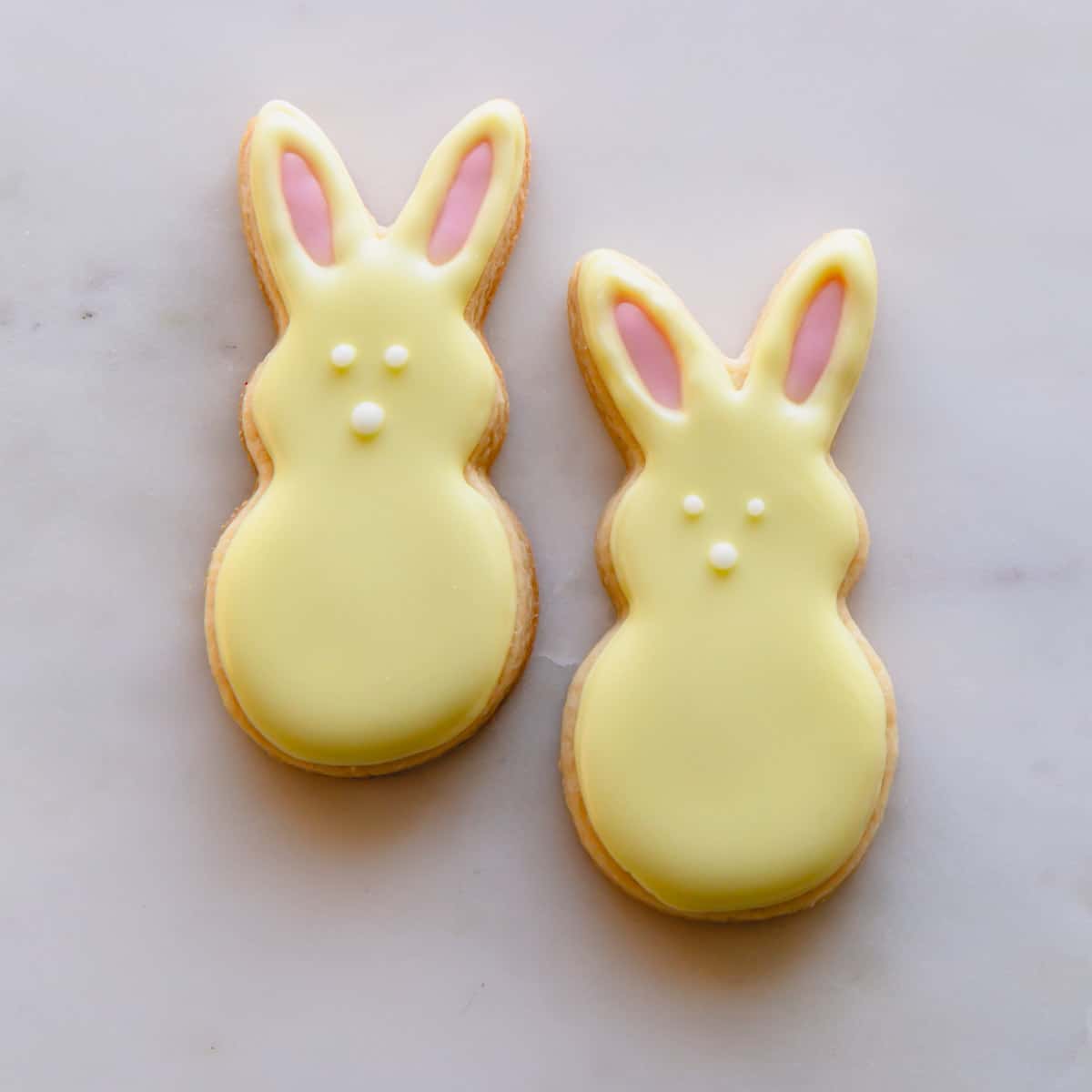 Two yellow Easter bunny sugar cookies with pink ears and white eyes and noses.