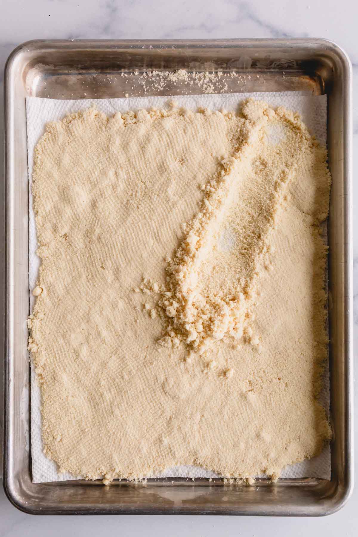 A layer of almond flour on a baking sheet lined with paper towel and some fluffe with a spoon.