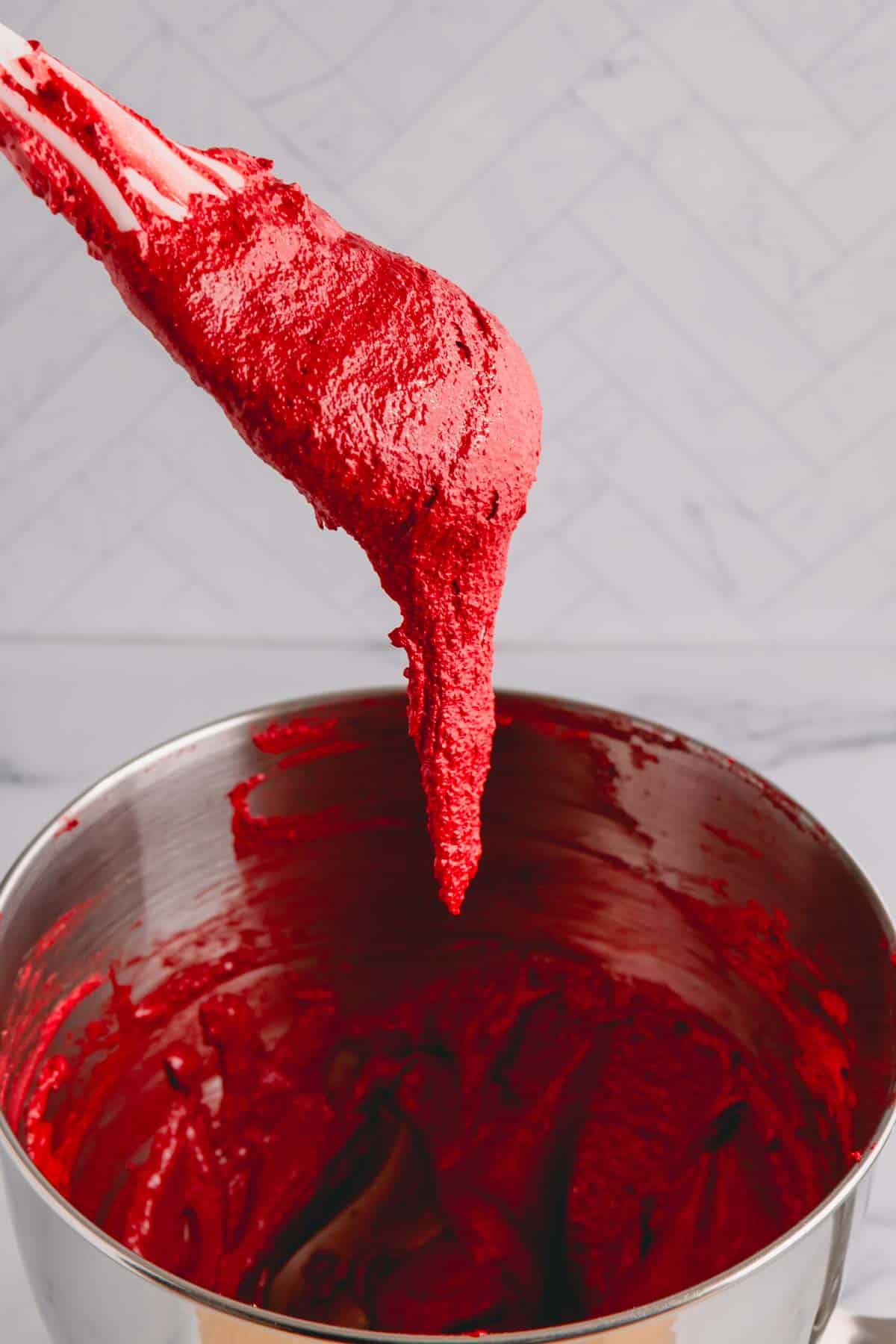 A spoonful of red macaron batter falling off the spatula into the mixing bowl.