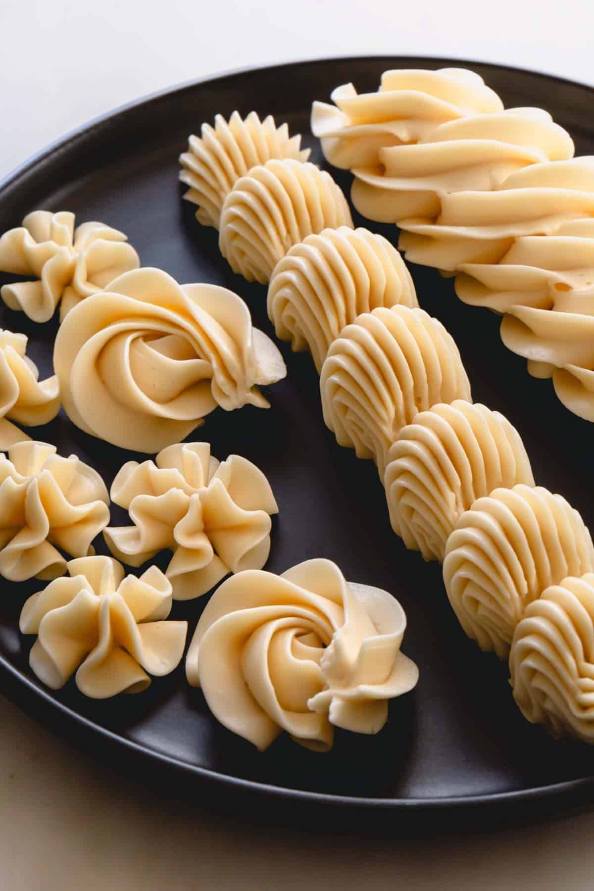 Piped designs of vanilla Russian buttercream on a black plate.