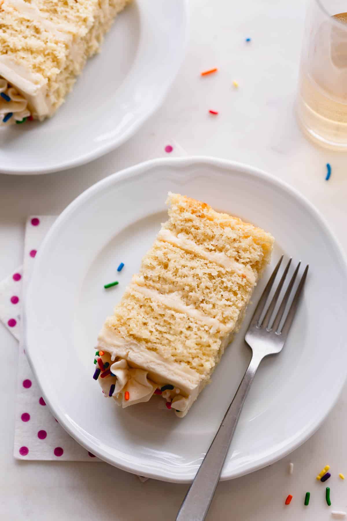 A slice of vanilla bean cake with vanilla Russian buttercream on a plate with a fork.