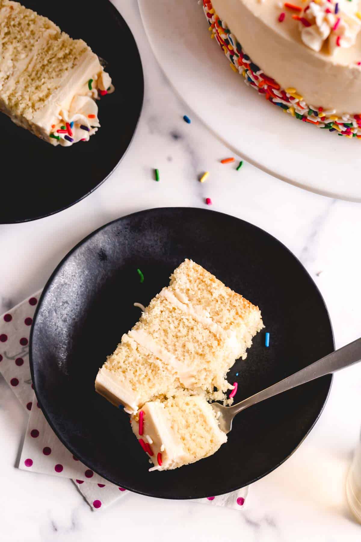 Slices of vanilla bean cake on black plates with a fork holding a bite.
