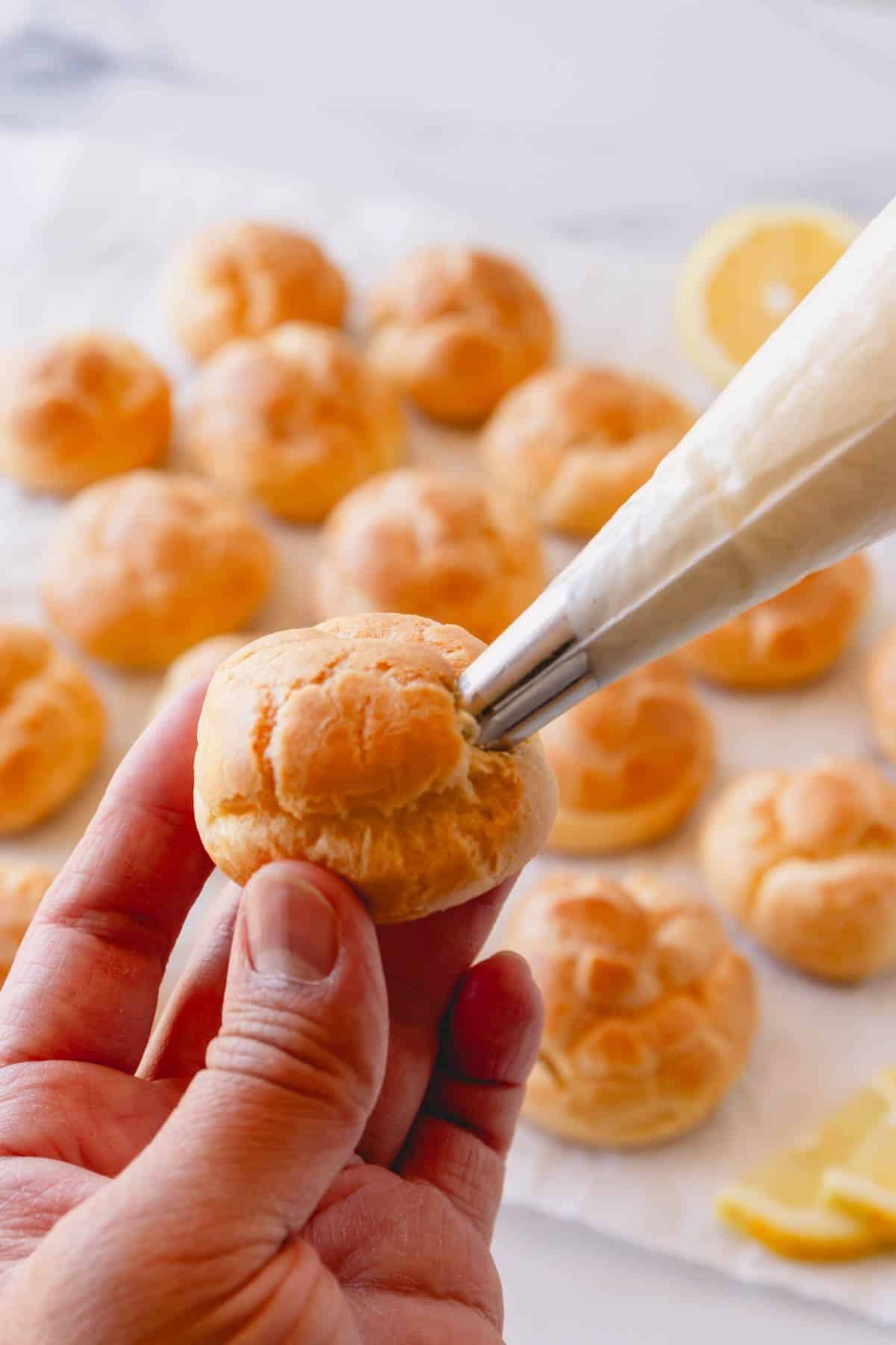 A creme puff being filled with lemon curd cream.