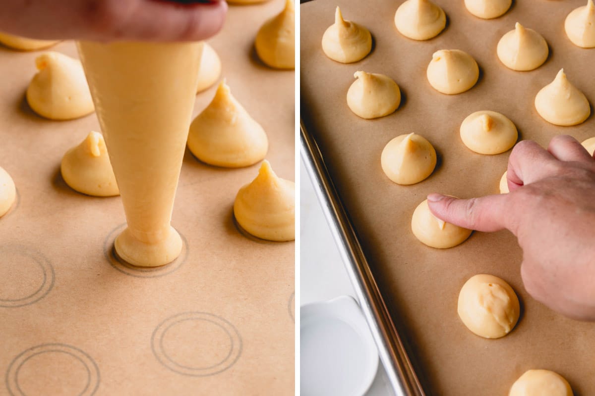 Creme puff dough being piped onto a baking sheet and a hand gently pressing the tops down.