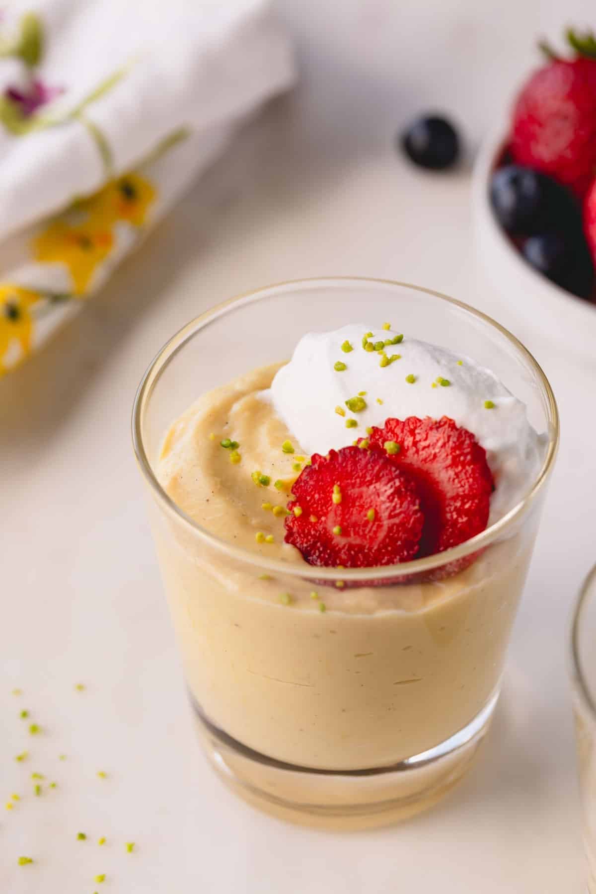 A cup of vanilla pudding topped with strawberries, whipped cream, and crushed pistachios.