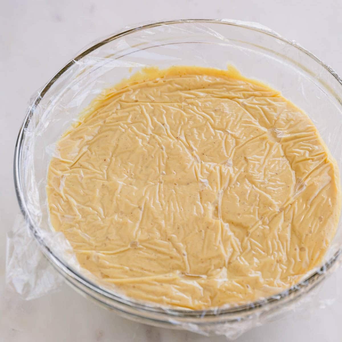 A bowl of vanilla pudding with plastic wrap covering the top.