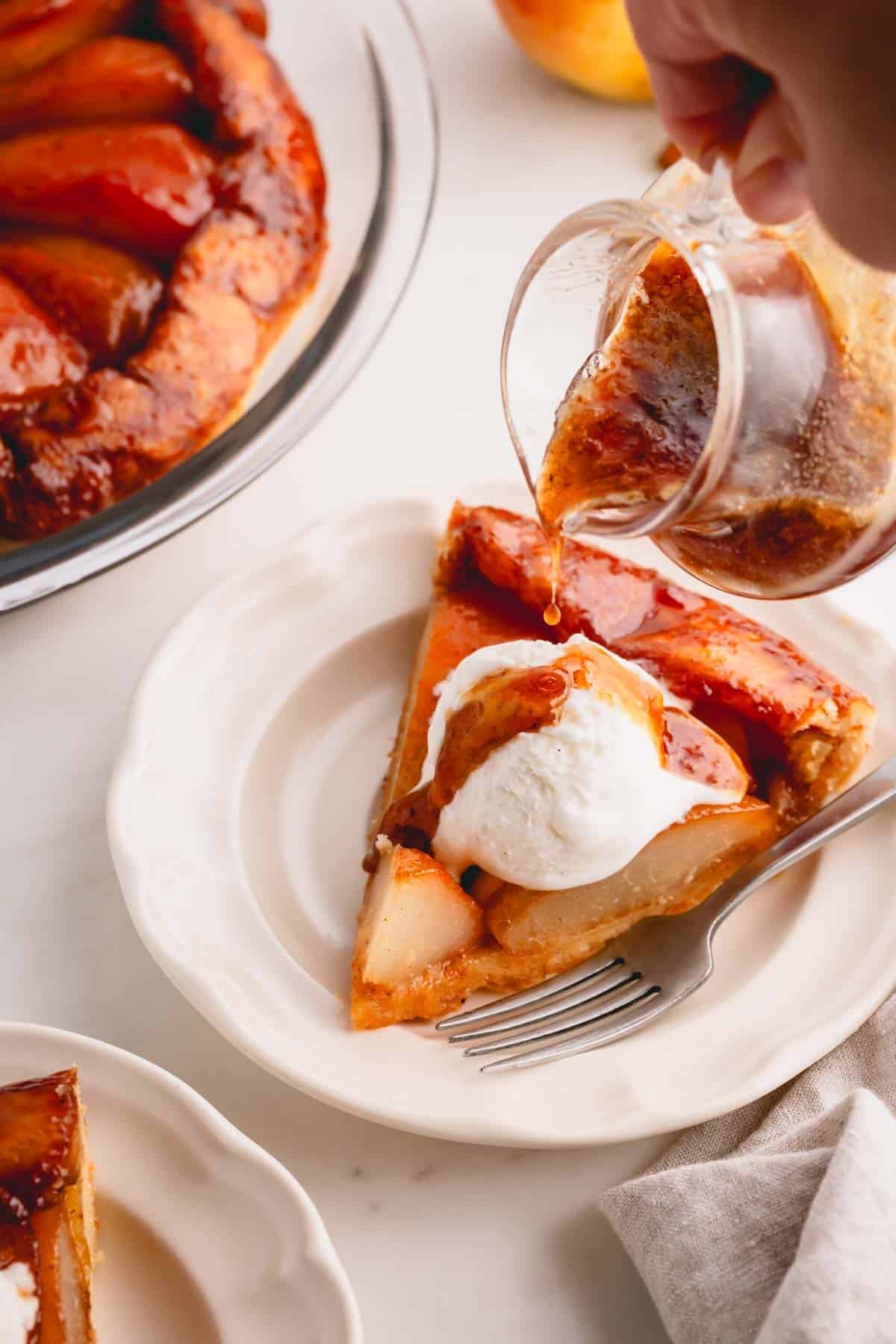 Pear syrup being poured over a slice of French pear pie topped with vanilla ice cream.