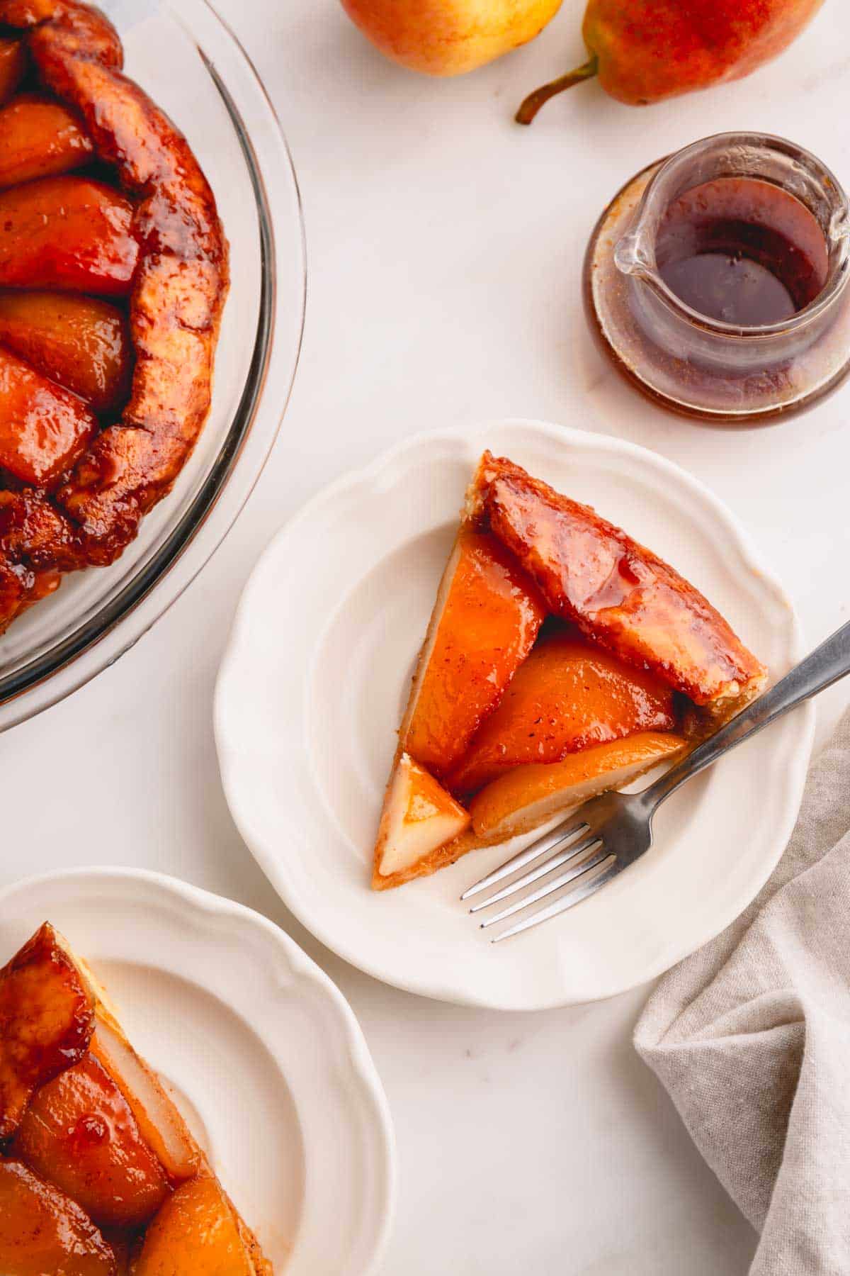 A slice of pear tarte tatin on a plate with a fork.