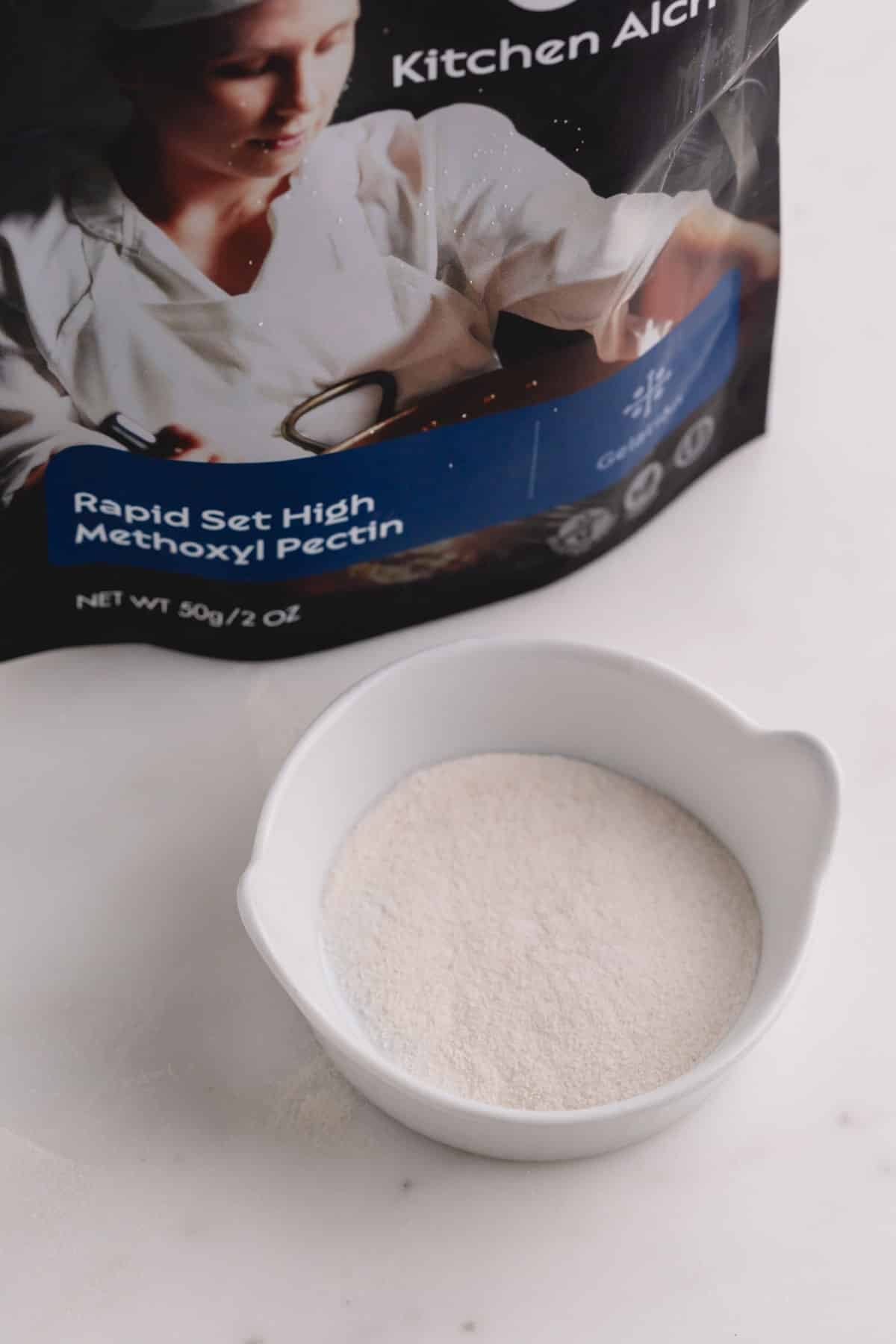 A small white dish filled with white pectin powder with the packet on the background.