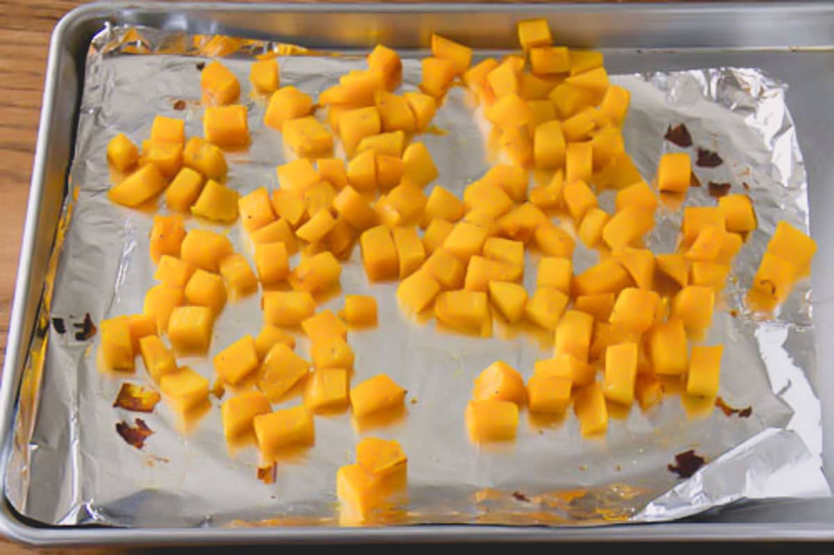 Cubed acorn squash on a baking sheet lined with a foil.