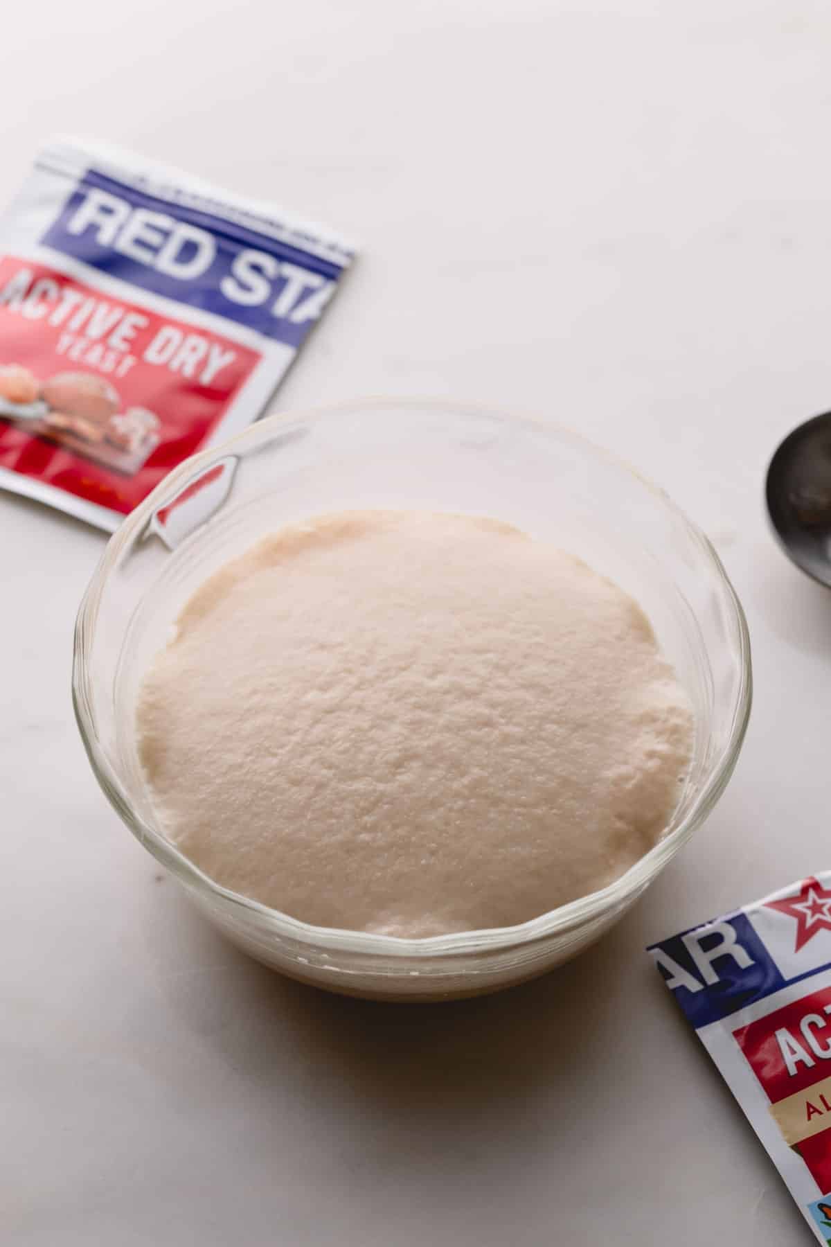 Yeast mixture is puffed in a small glass bowl with a packet of active dry yeast in the background..