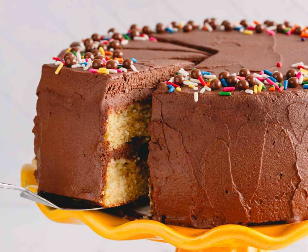 A slice of chocolate frosted yellow cake being lifted from a yellow cake stand.