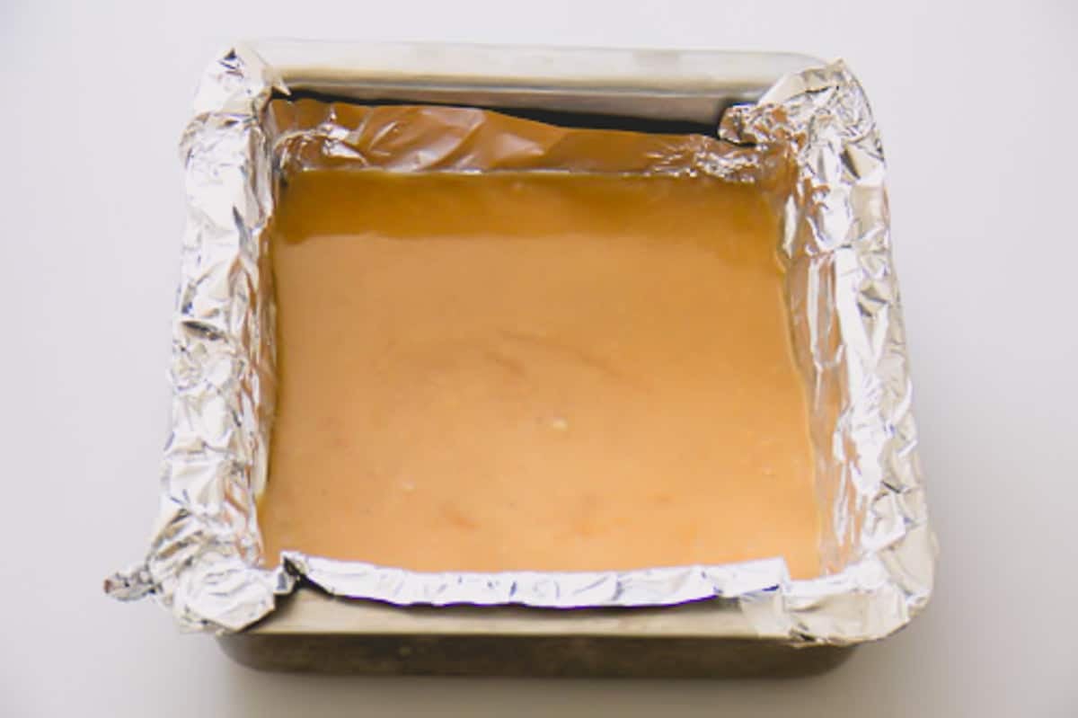 Cardamom caramel candies cooling in a square baking dish lined with aluminum foil.