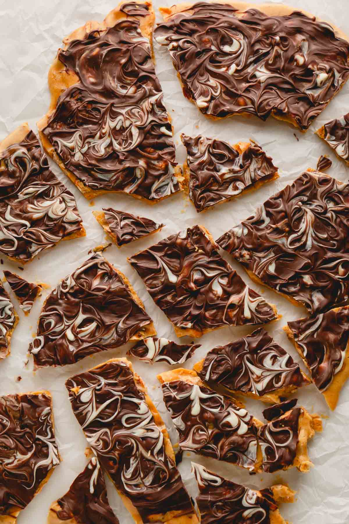 Overhead image of chocolate peanut brittle pieces on parchment paper.