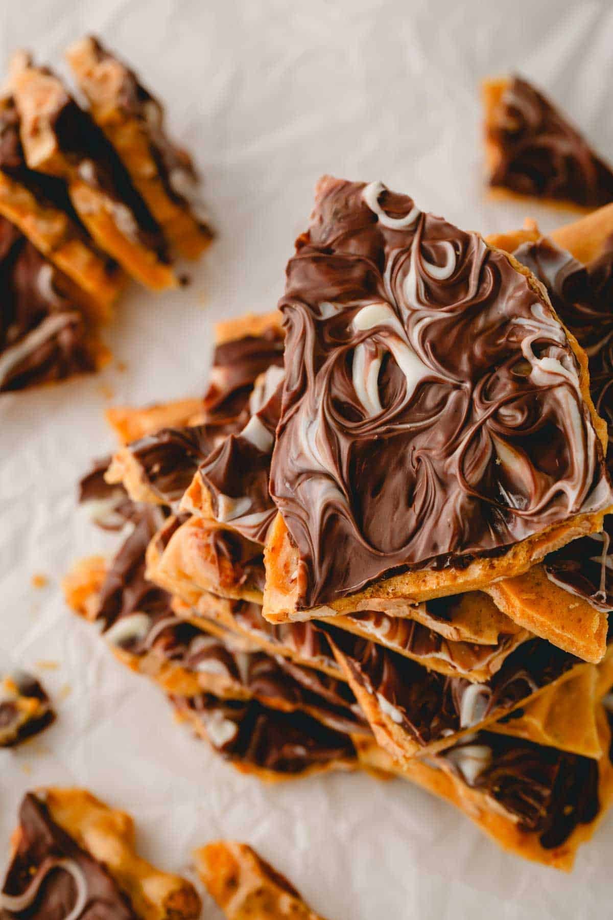 Overhead image of chocolate peanut brittle pieces with a white chocolate swirl.