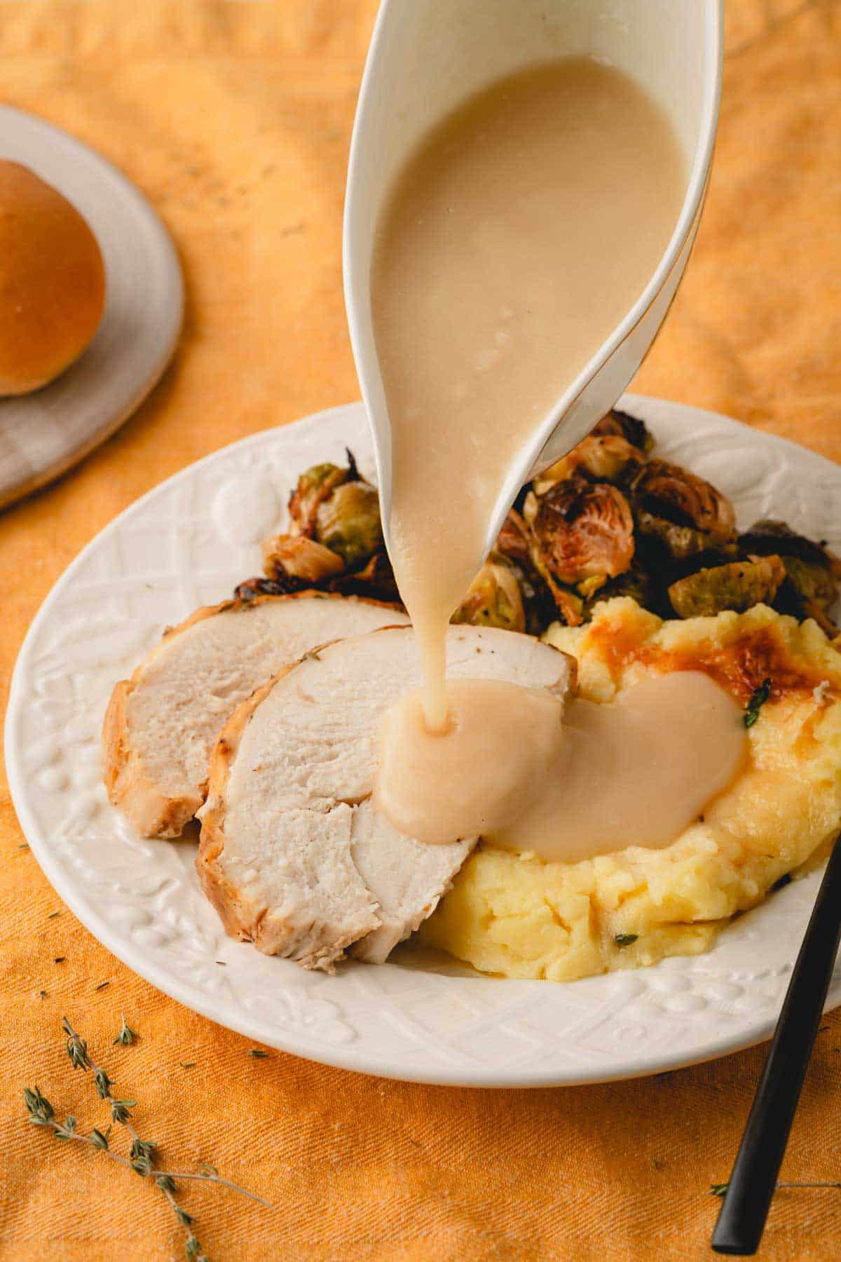 Turkey gravy being poured over turkey slices on a plate.