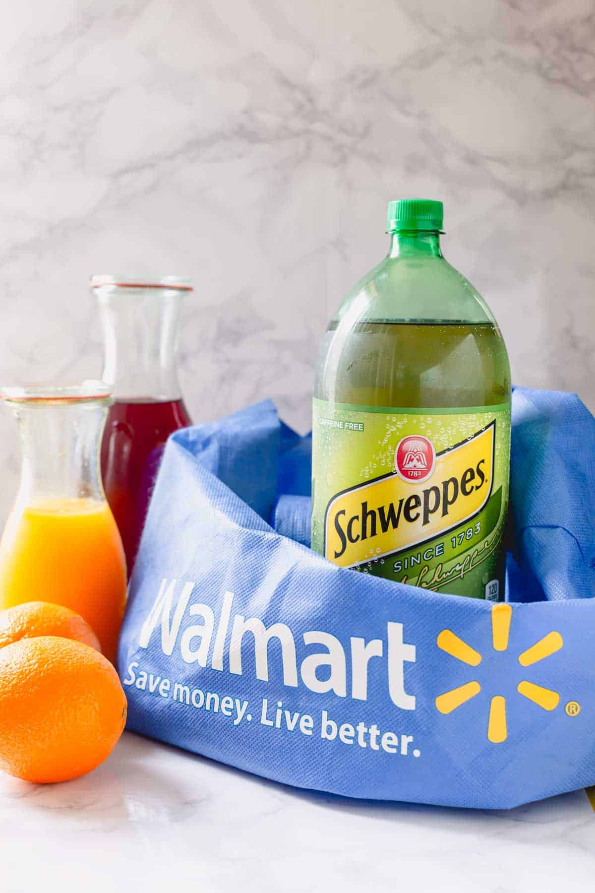 Schweppes ginger ale, two oranges, orange juice, and pomegranate juice with a Walmart bag.