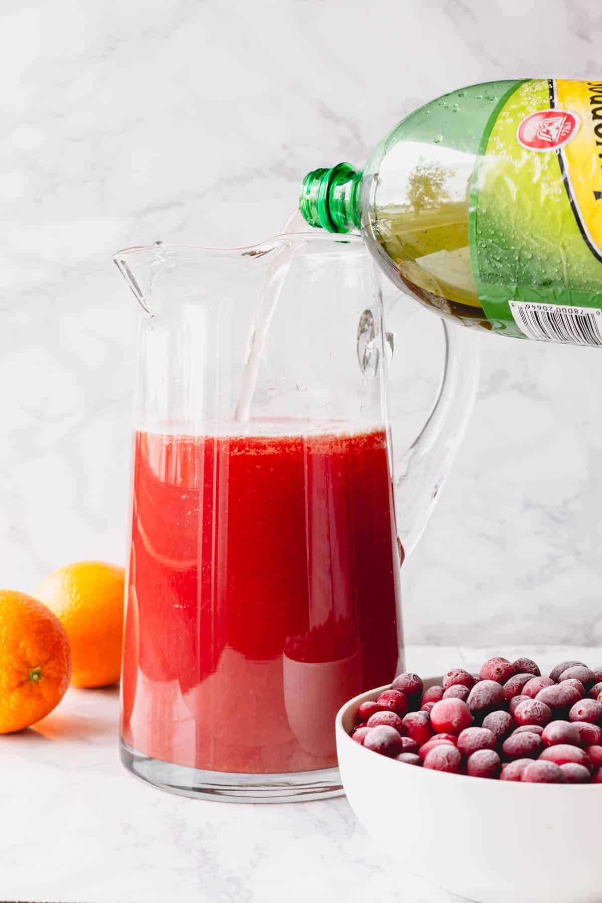 Ginger ale being poured into a pitcher of orange juice and cranberry juice.