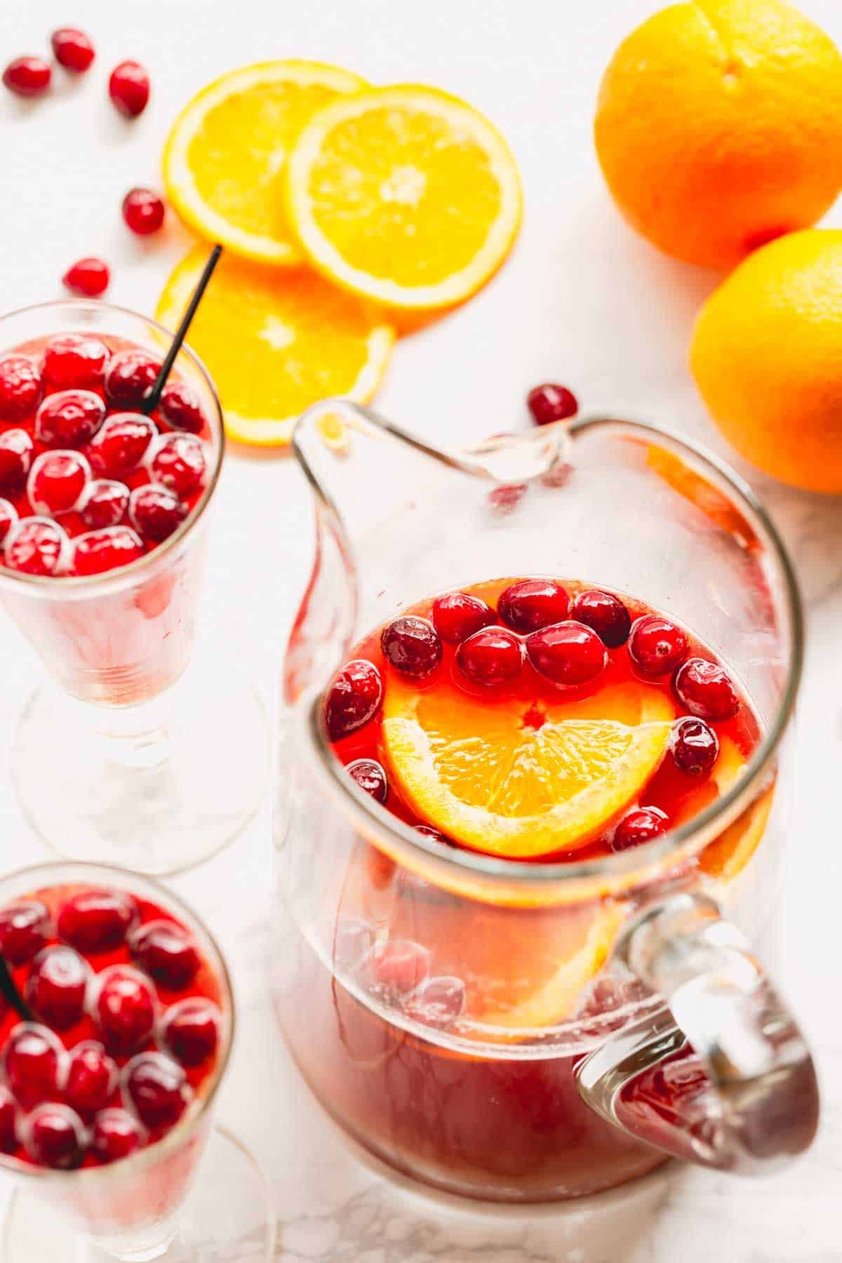 Overhead image of two glasses of orange cranberry spritzer and a pitcher of the spritzer mix.