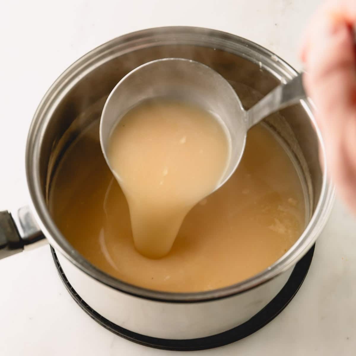 Turkey gravy in a saucepan and the gravy being lifted with a ladle.