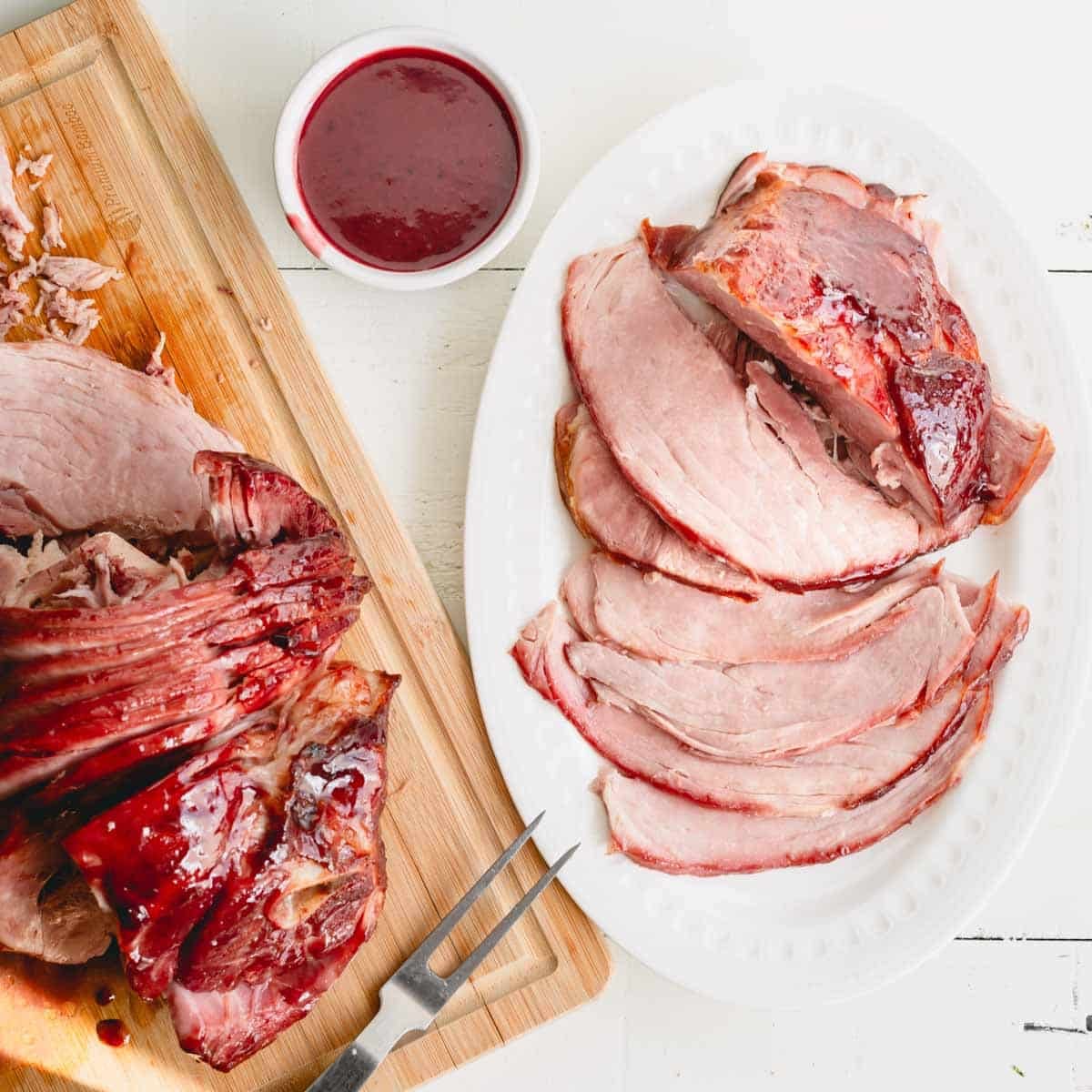 Overhead image of glazed spiral ham on a wooden cutting board and a serving platter with a bowl of glaze.