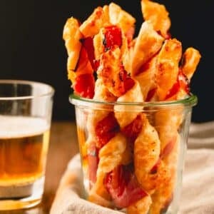 Savory puff pastry twists in a glass cup.