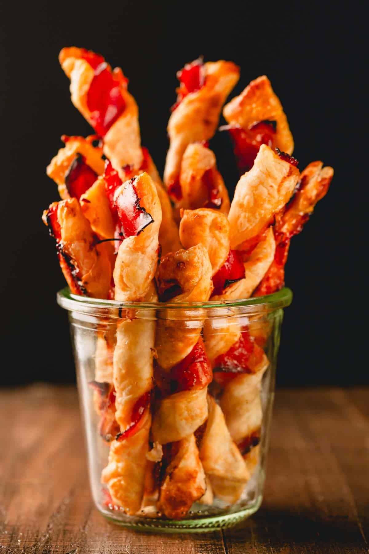 A glass jar full of baked puff pastry twists with prosciutto.