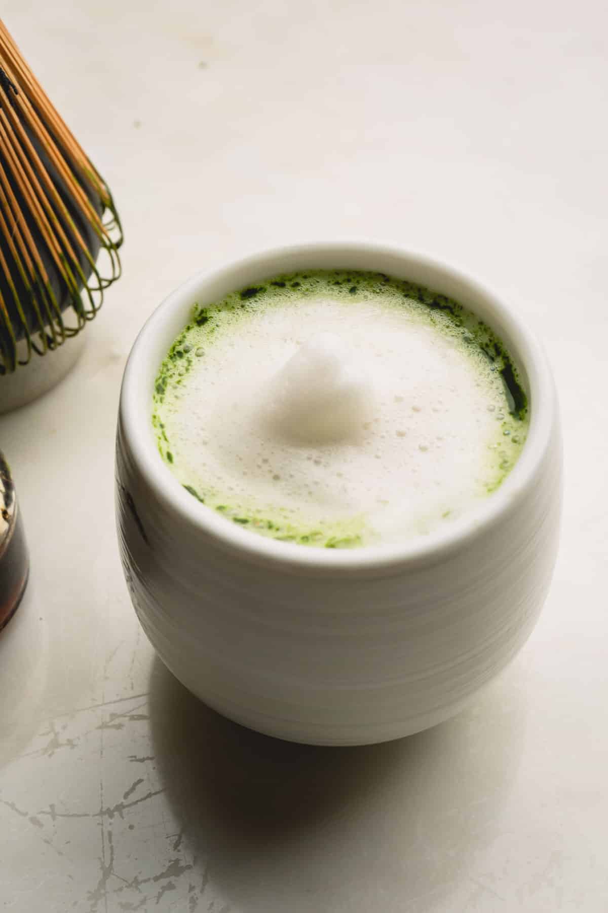 Matcha latte in a small cup topped with white foam.