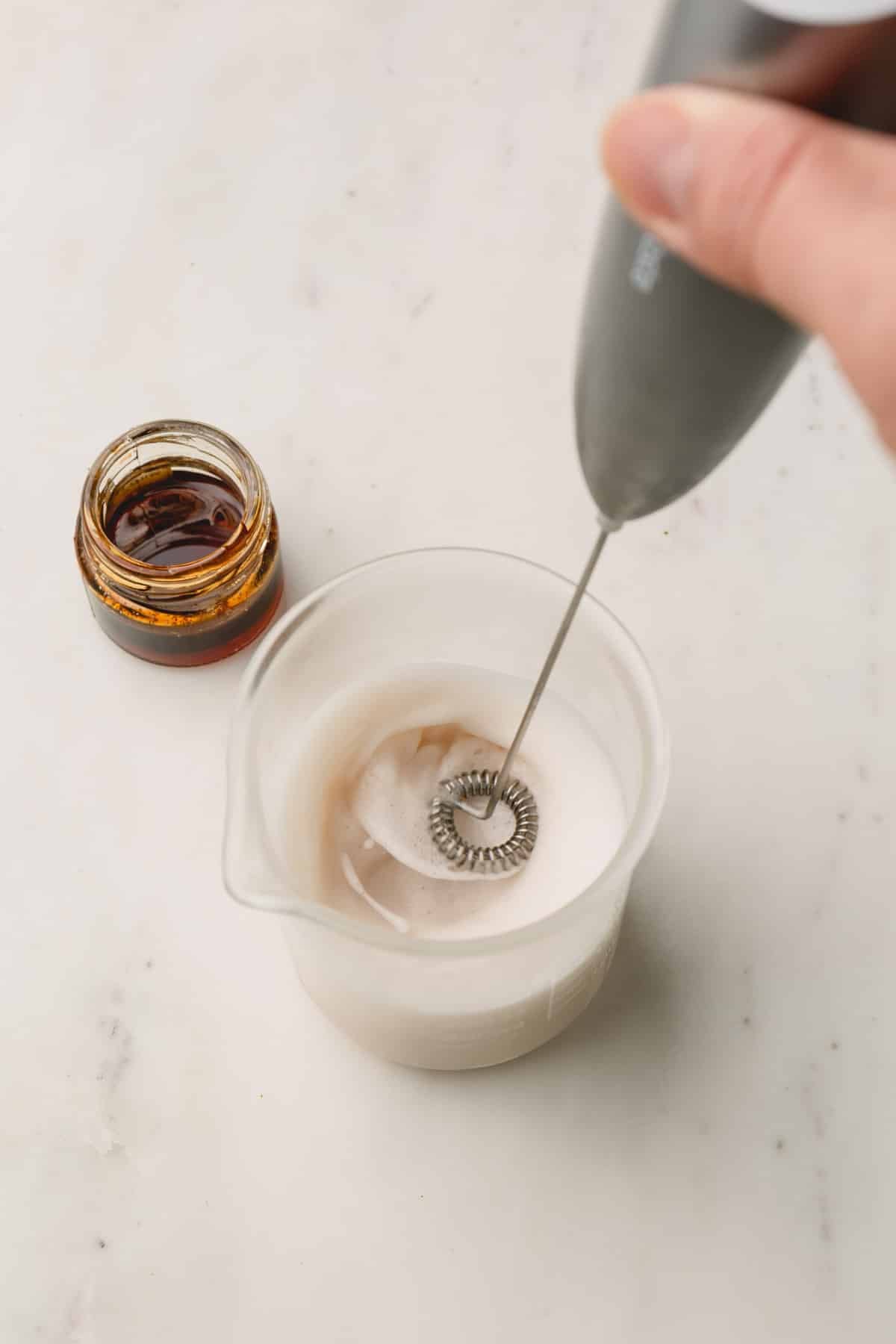 A glass of milk is stirred with a handheld milk frother.