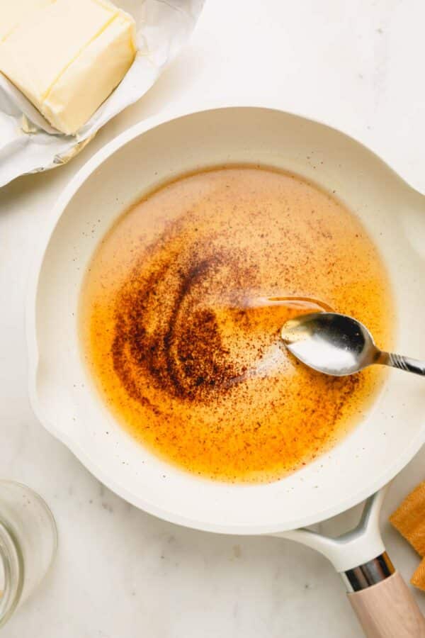Melted brown butter in a white skillet with a spoon swirling the butter.