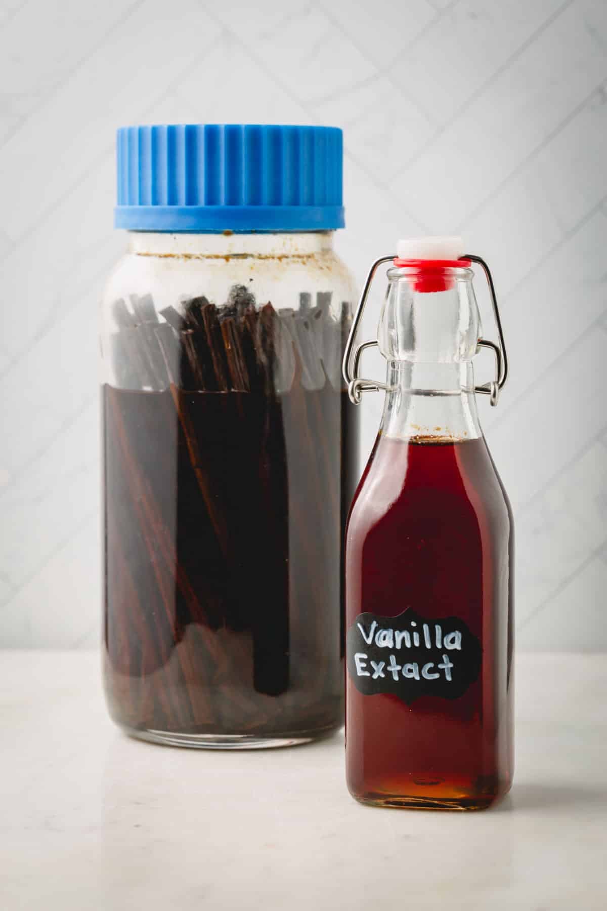 Big jar of homemade vanilla extract with vanilla beans and a smaller bottle of vanilla extract.