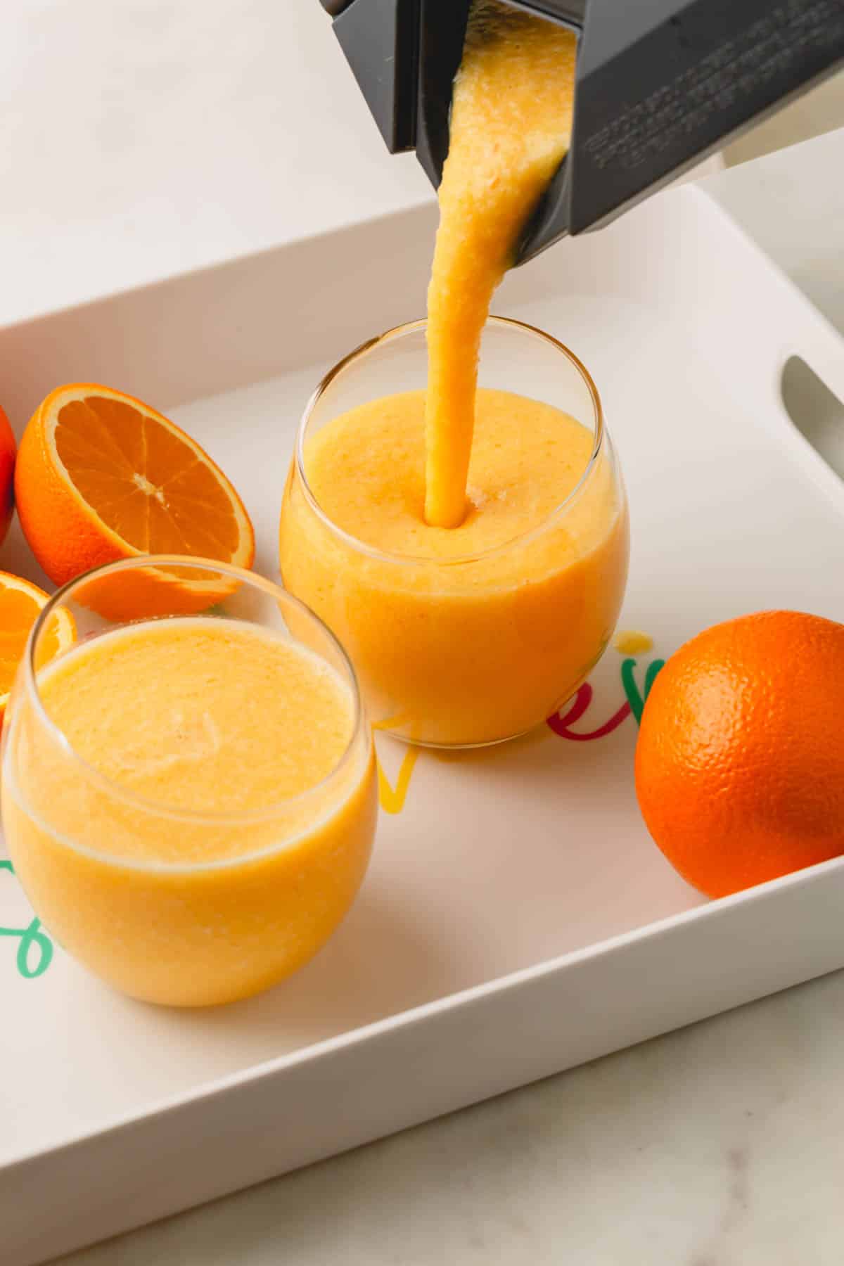 A coconut orange Julius drink being poured into two glasses from a blender.