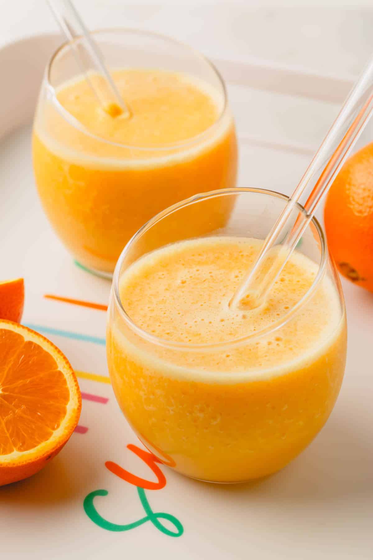 Two glasses of a coconut orange Julius drink with glass straws.