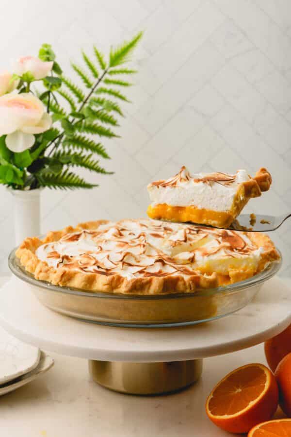 A slice of orange meringue pie being lifted from a pan full of the rest of the pie.