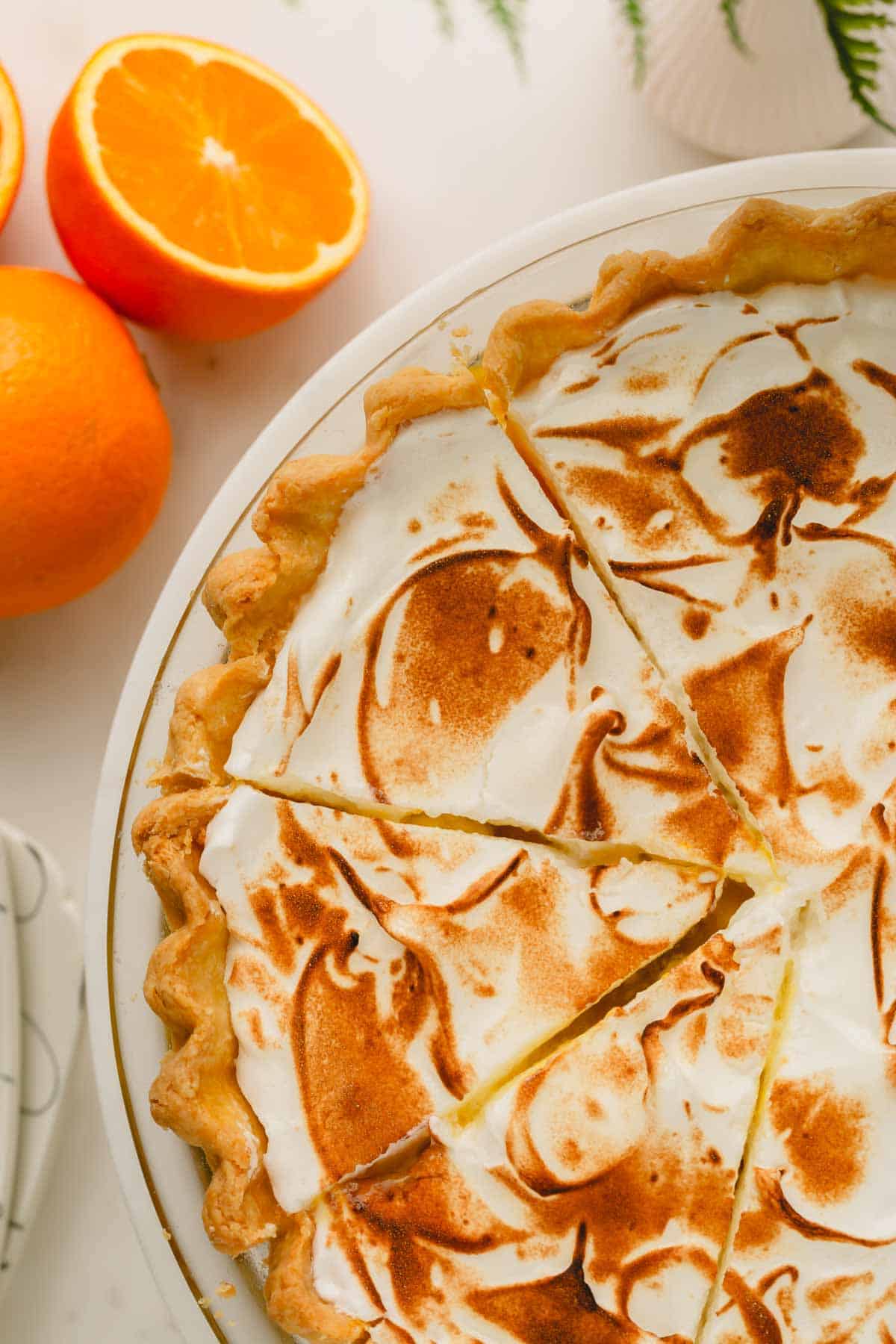 An orange meringue pie cut into slices on a platter with oranges next to it.