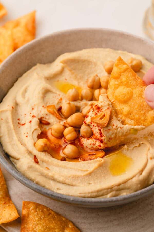 A chip being dipped into a bowl of roasted garlic hummus.
