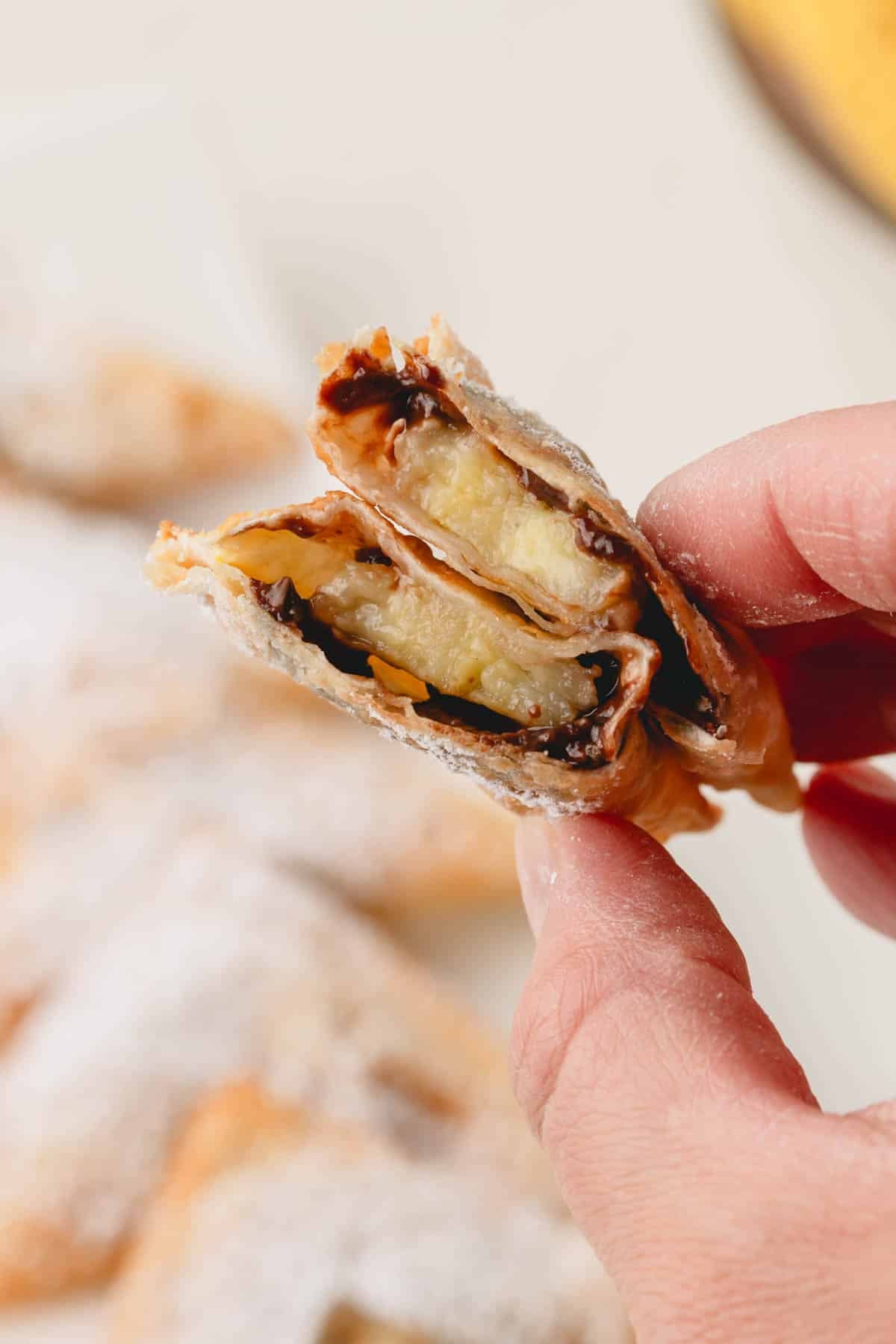 A hand holding a banana Nutella wonton split in half.