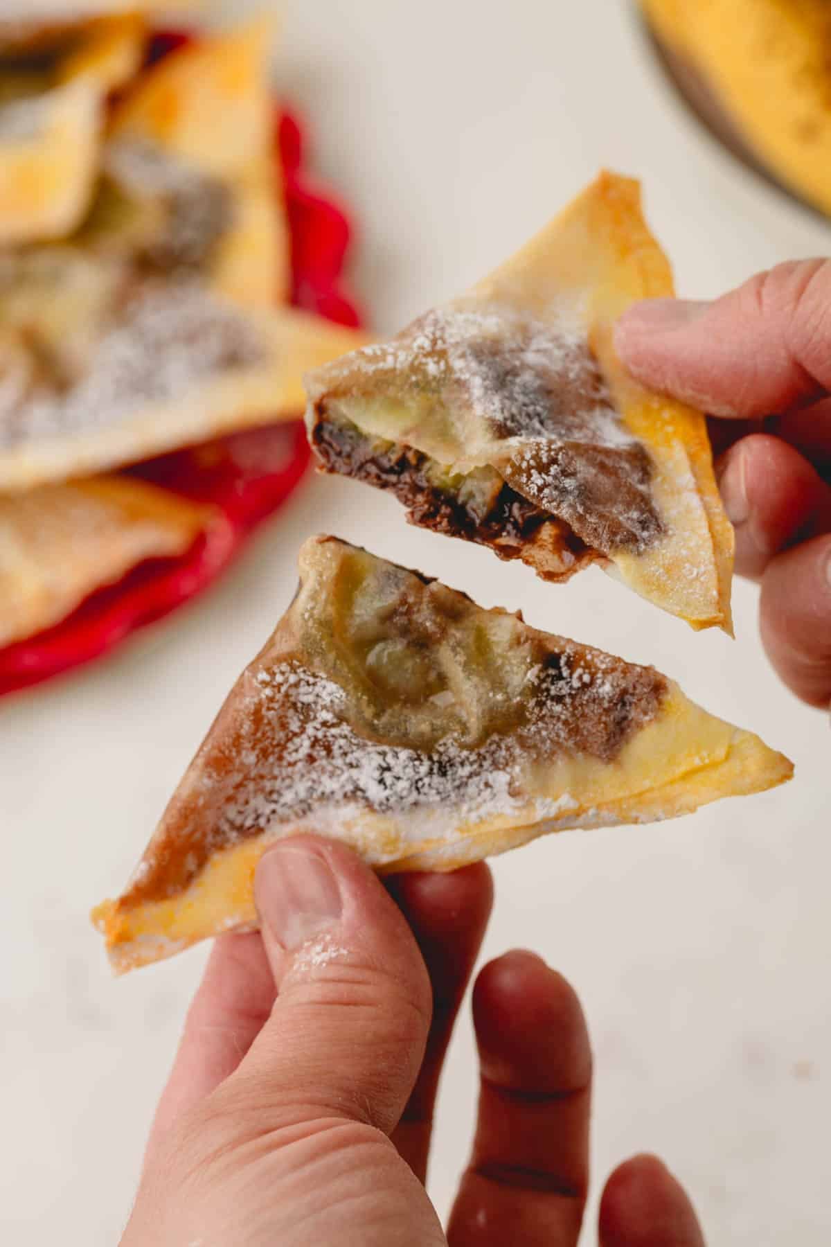 Two hands, each holding a half of a banana Nutella wonton.