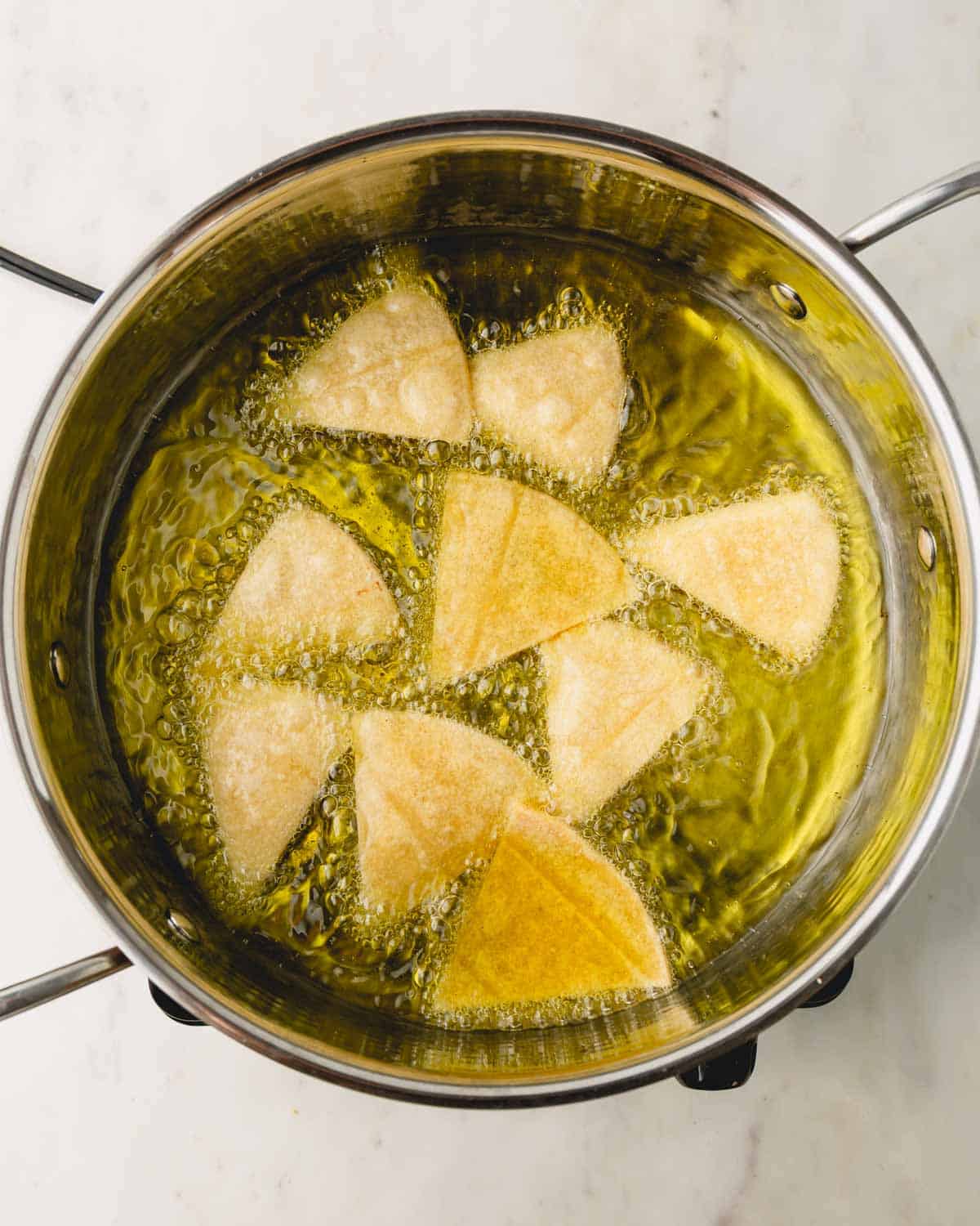 Tortilla chips frying in a pot of oil.