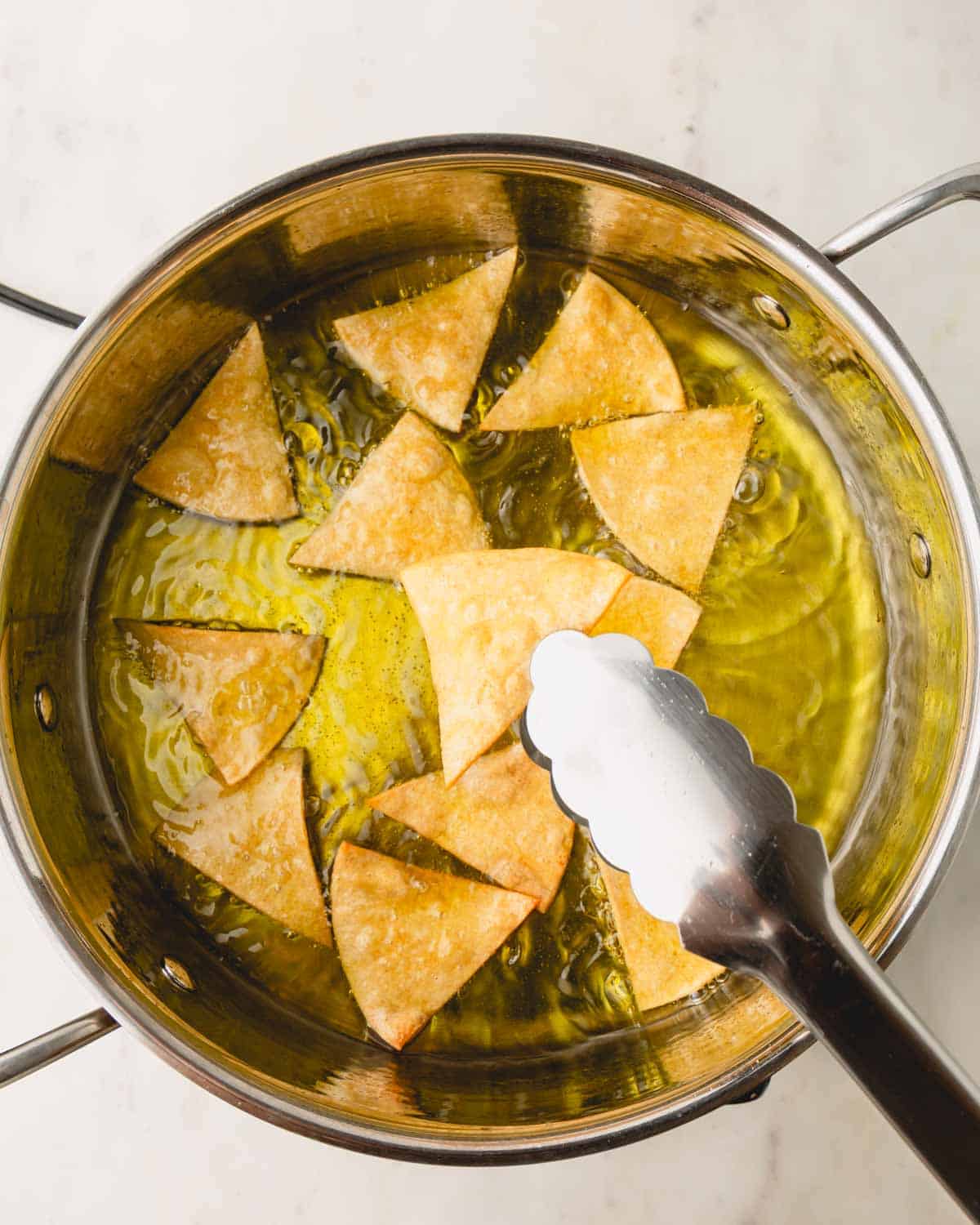Tongs removing tortilla chips from a pot of oil.