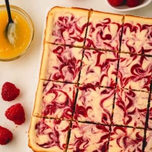 Lemon raspberry cheesecake bars next to fresh raspberries and a bowl of lemon curd.