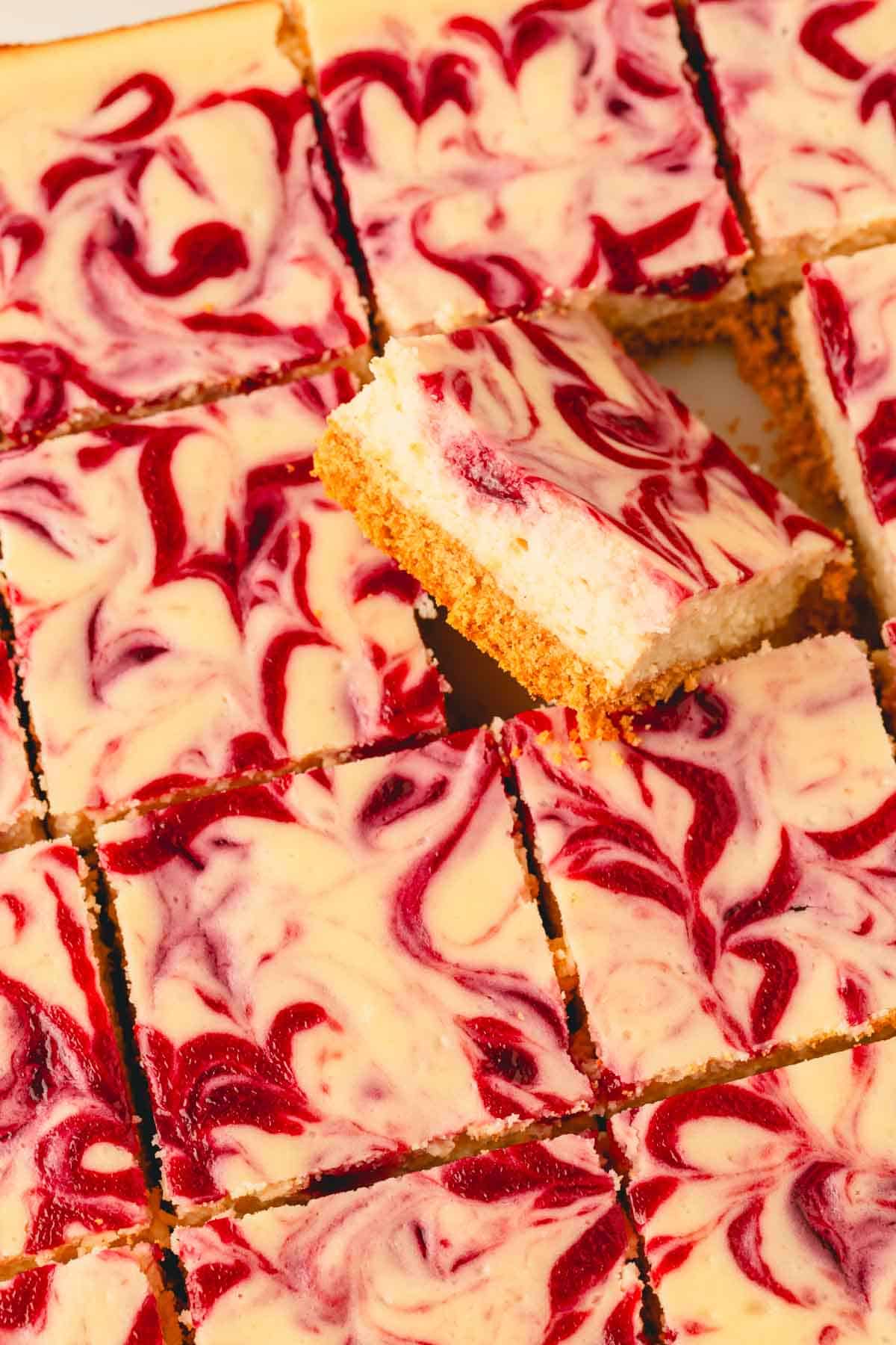 Lemon raspberry cheesecake bars, one tipped to the side exposing a graham cracker crust.