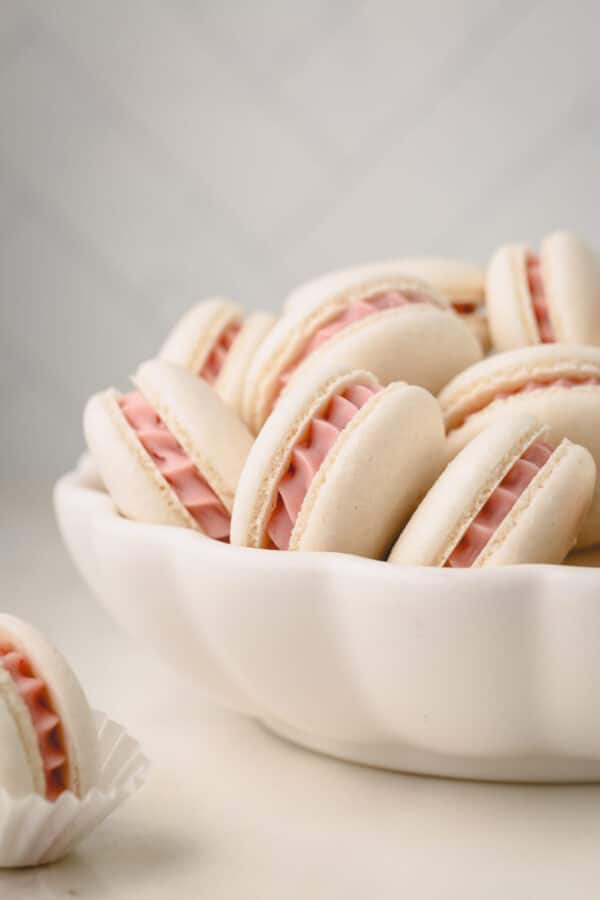 A bowl of vegan macarons with a strawberry ganache filling.