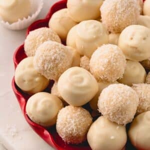 A red platter with white chocolate coated and desiccated coconut coated almond coconut balls.