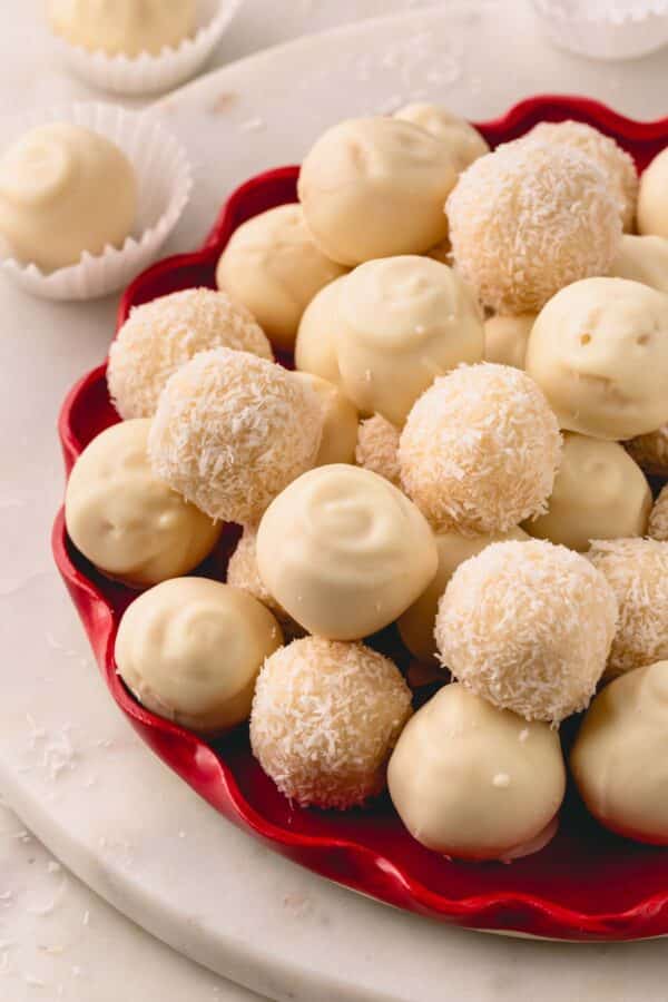 A red platter with white chocolate coated and desiccated coconut coated almond coconut balls.