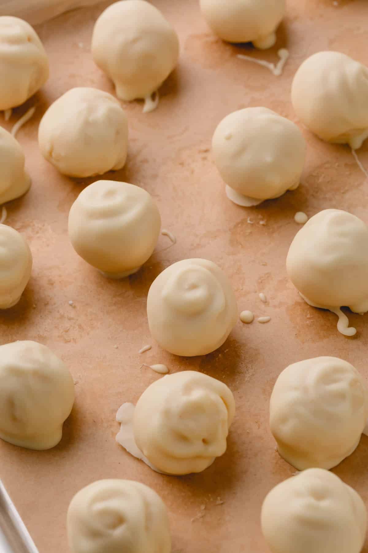 White chocolate covered coconut balls on a parchment paper-lined baking sheet.