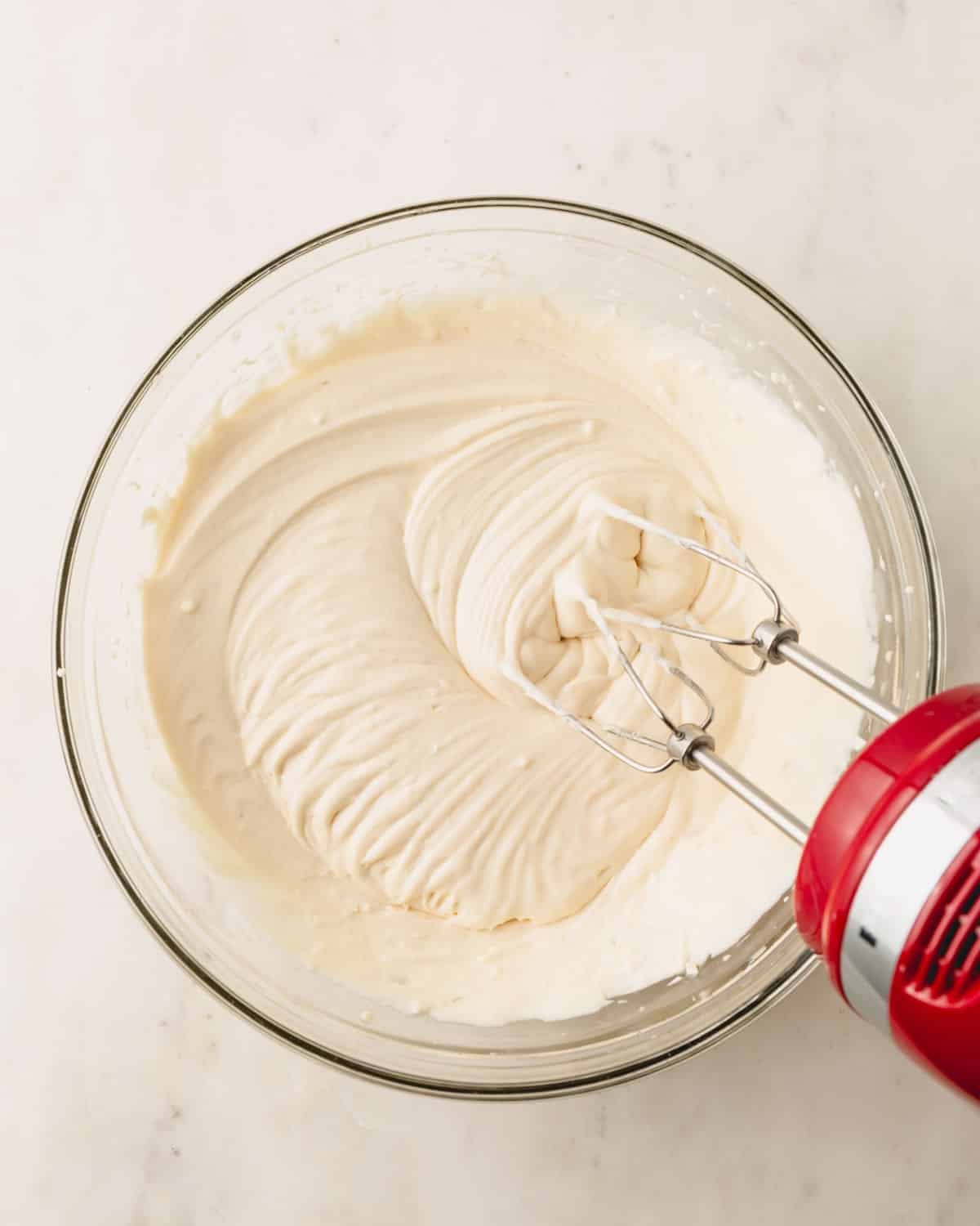 A bowl of whipped heavy cream with a hand mixer sticking out.