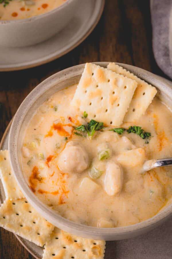 A bowl of oyster stew with a spoon and two crackers sticking out.