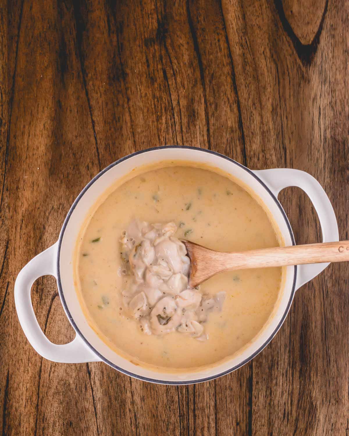 Oysters being added to a pot of stew with a wooden spoon sticking out.